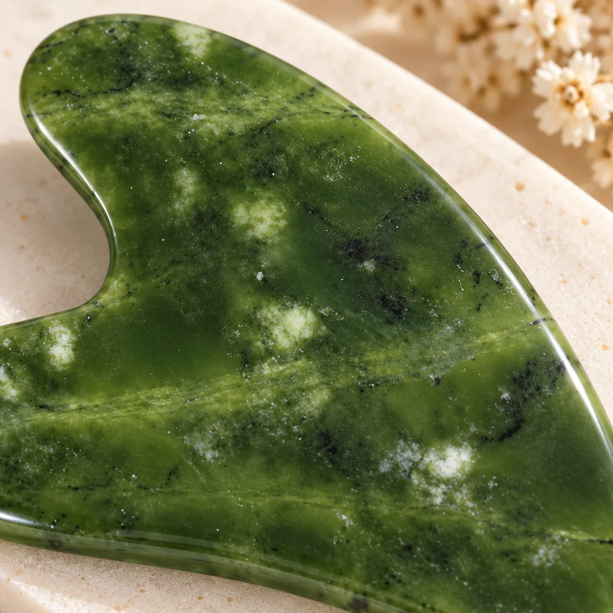 Gua sha en jade, plaque de néphrite polie, gros plan sur le grain et la translucidite de la pierre